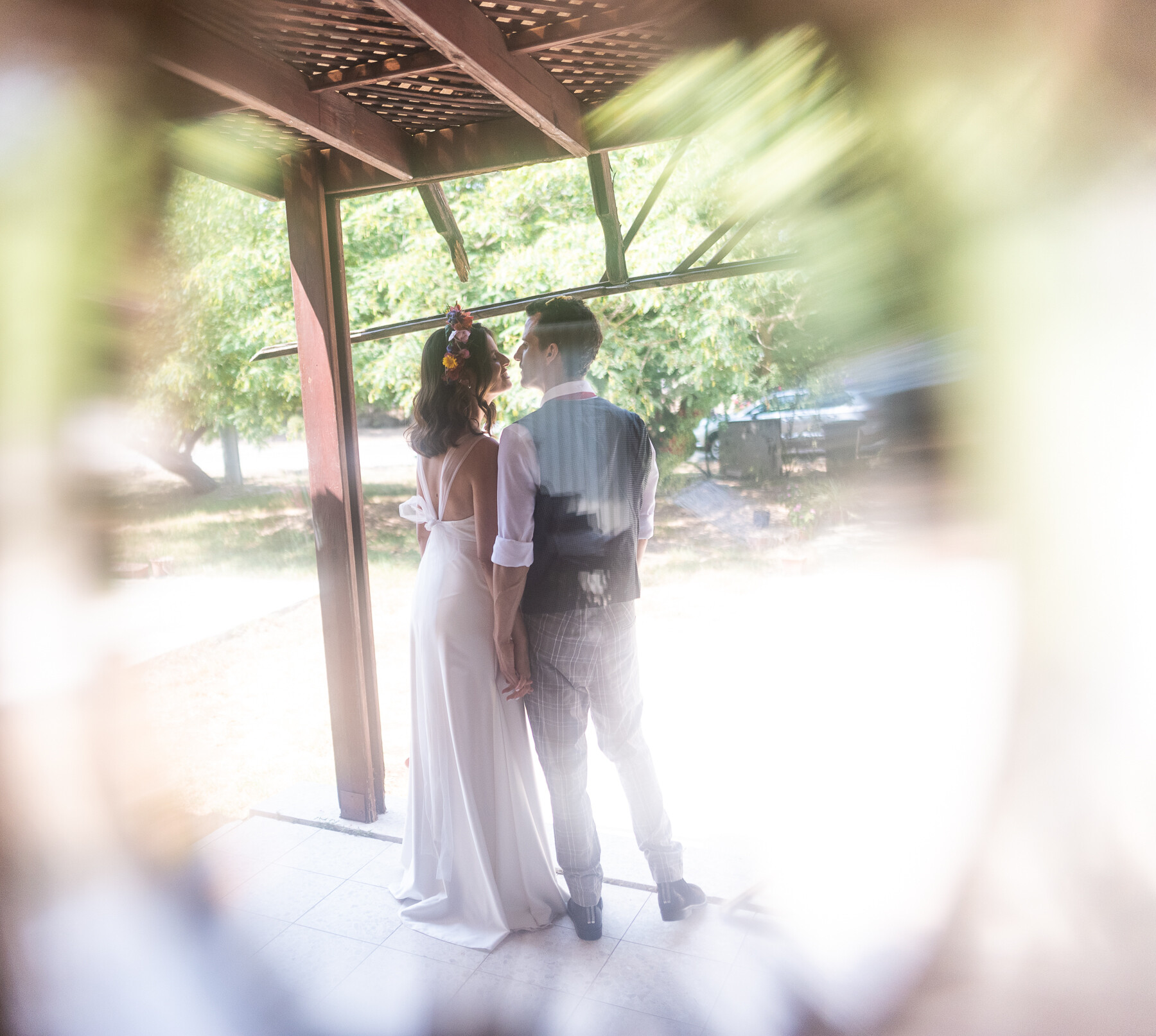 Backlit couple standing close under a wooden pergola