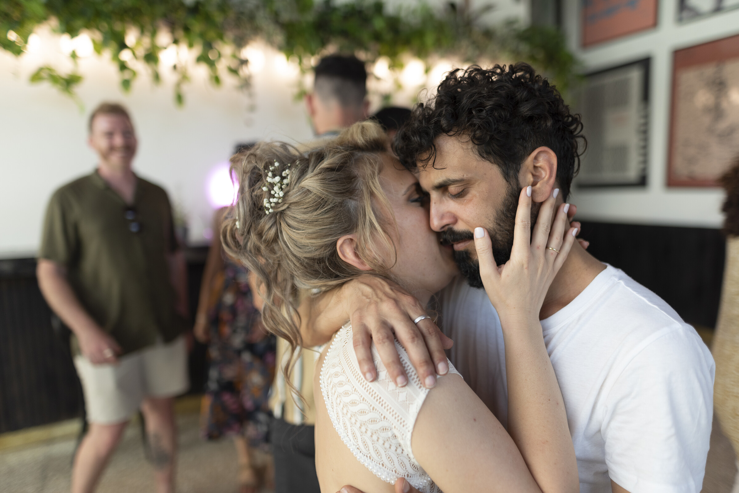 Close embrace on the dance floor, string lights and greenery overhead
